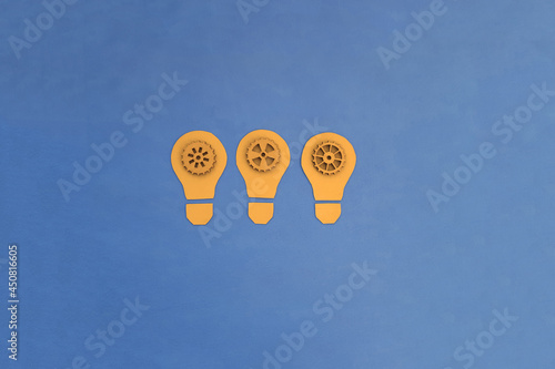 Obraz na płótnie Electric light bulbs are yellow, inside there are wooden gears of blue color on a blue background. Ideas, creativity. w salonie