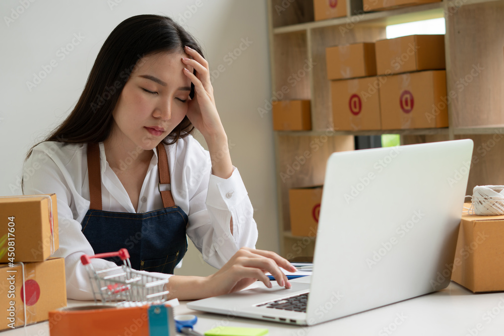 Small business entrepreneur who started an SME. Young Asian woman working on a laptop computer. Feeling stressed from the declining sales Small business entrepreneur who started an SME. Young Asian woman working on a laptop computer. Feeling stressed from the declining sales