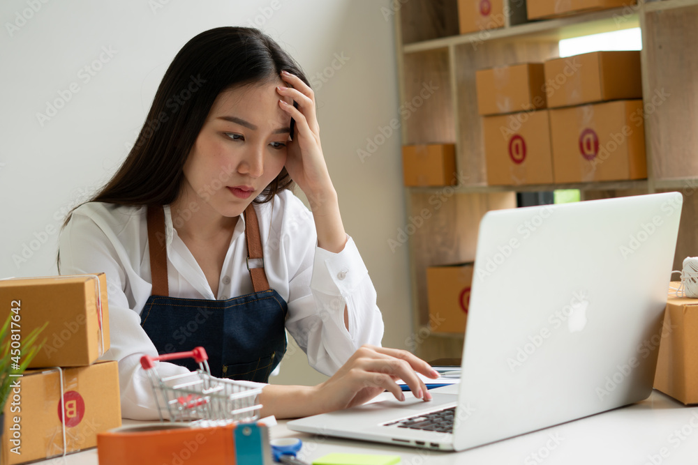 Small business entrepreneur who started an SME. Young Asian woman working on a laptop computer. Feeling stressed from the declining sales Small business entrepreneur who started an SME. Young Asian woman working on a laptop computer. Feeling stressed from the declining sales