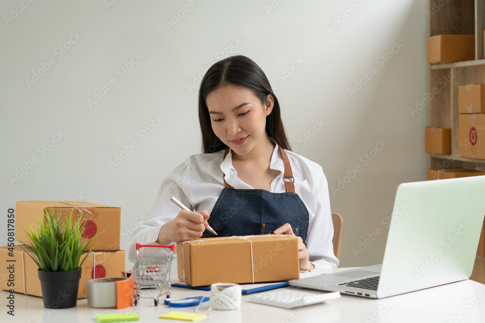 Startup small business entrepreneur SME, young asian woman working with laptop computer and delivery packaging box, online market packing, SME e-commerce seller concept. Startup small business entrepreneur SME, young asian woman working with laptop computer and delivery packaging box, online market packing, SME e-commerce seller concept.