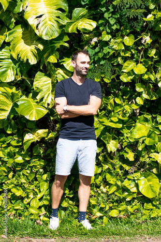 Caucasian man wearing blue shorts and a blue t-shirt looking to the side over a green natural background