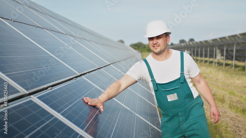 Portrait of proud worker industrial engineer in uniform standing on field with large solar batteries. Ecological farm. Solar power station. People. Sustainable energy. Solar power field. Ecology.