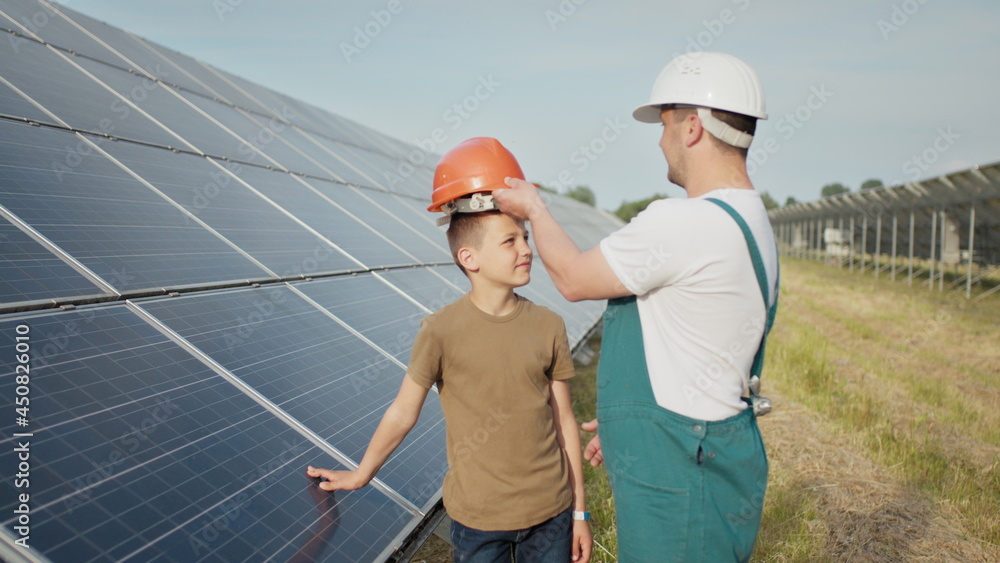 An young engineer father is explaining to his little son an operation and performance of photovoltaic solar panels at sunset. Concept: renewable energy, technology, electricity, green, future, family. An young engineer father is explaining to his little son an operation and performance of photovoltaic solar panels at sunset. Concept: renewable energy, technology, electricity, green, future, family.