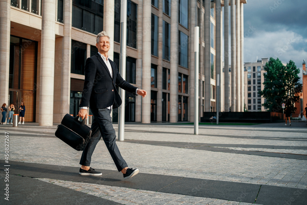 The lawyer holds a bag with documents in his hand. A successful entrepreneur goes to work in the morning. A manager in a business suit. Male freelancer fashionable hairstyle gray hair.