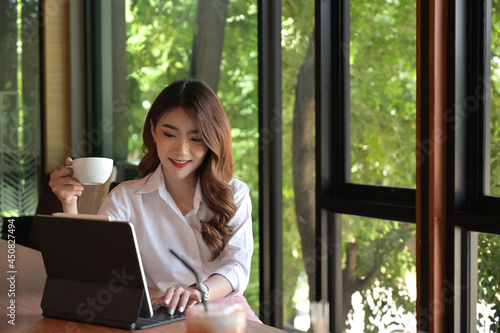 Front view with businesswoman working with tablet on the table and other hand holding a cup of coffee in meeting room.