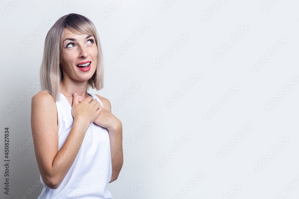 Smiling young woman holding her hands on her chest looking to the side on a light background Smiling young woman holding her hands on her chest looking to the side on a light background