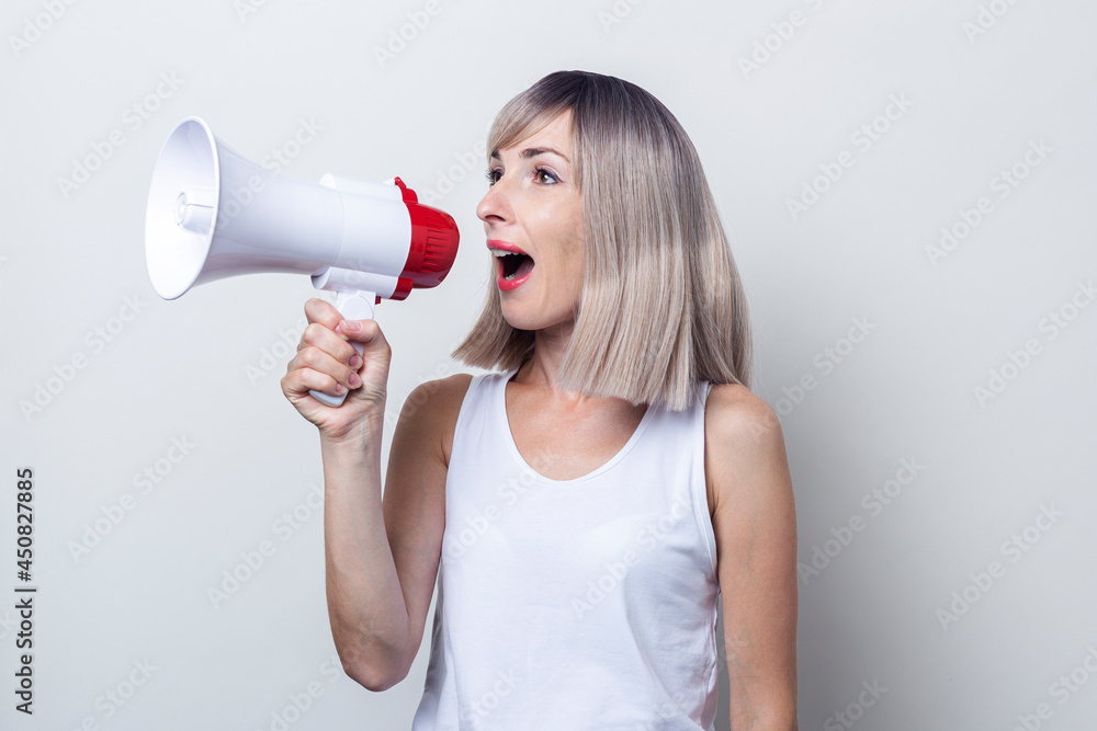 Young blonde woman shouts into a megaphone on a light background Young blonde woman shouts into a megaphone on a light background