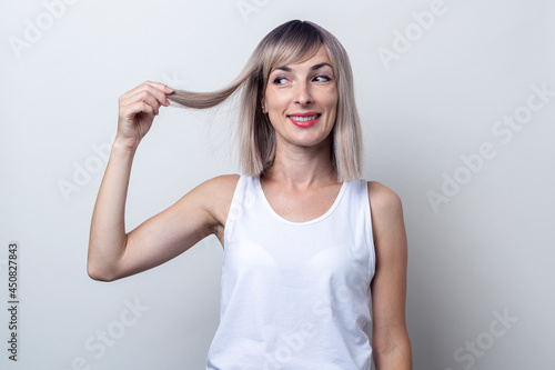 Wallpaper Mural Smiling young blonde woman looking at holding a lock of hair on a light background Torontodigital.ca