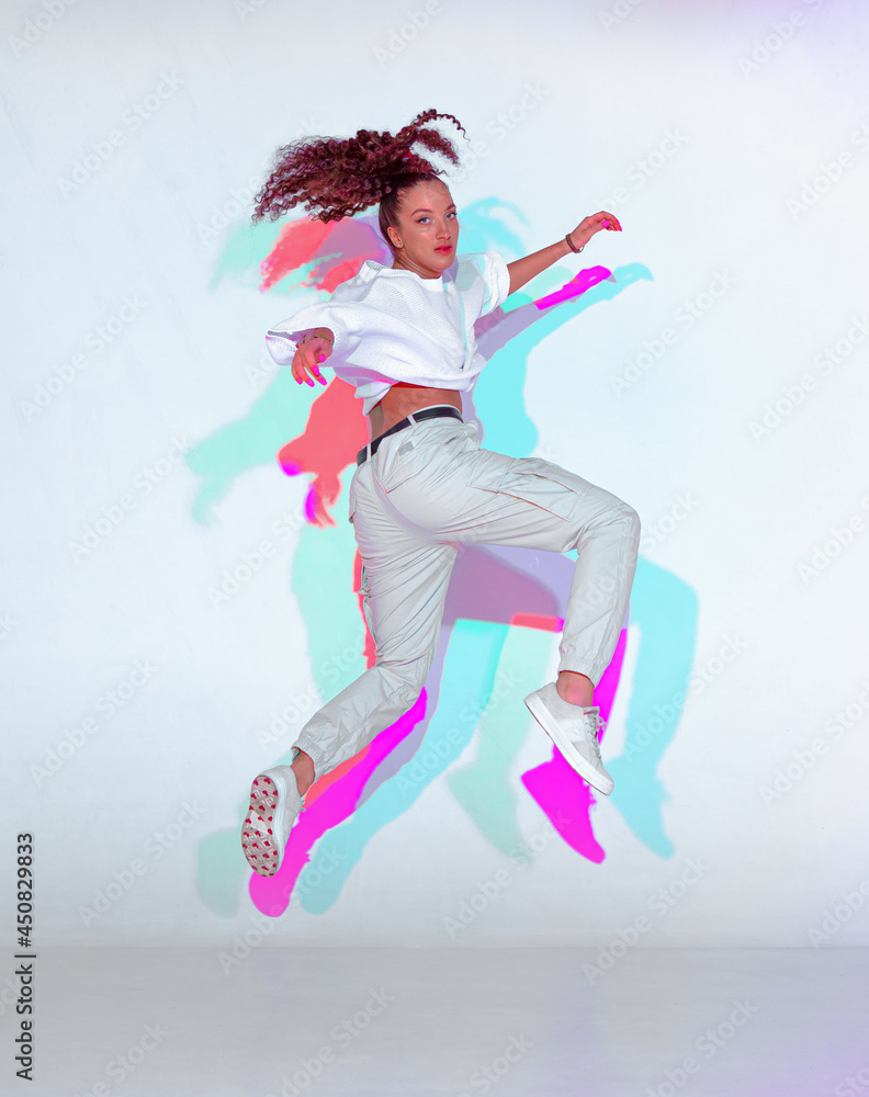 Jumping mixed race young girl dance in colourful light. Female dancer performer jump dancing fiery hip hop