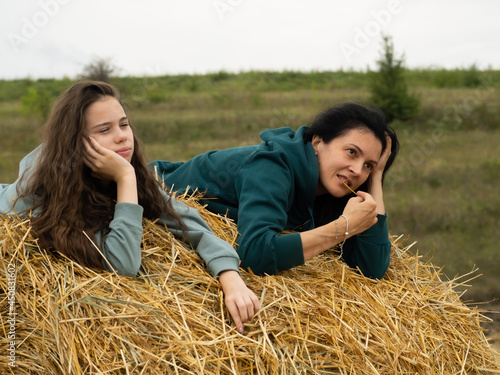 Happy teenage girl and girl relaxing on a hay bale field during harvest and enjoying a warm day outdoors. Lie on a wheat field on a summer day.