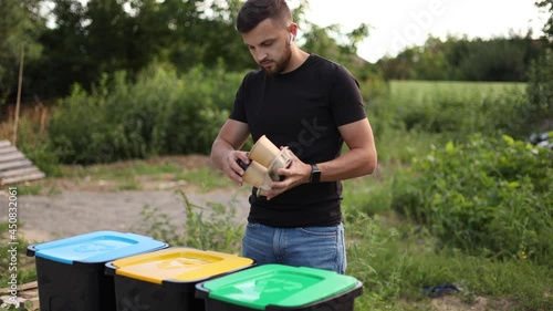 Man throwing out in the recycling bin disposable cup. Attractive young guy separate plactic lid with cardboard cup and thow into different bin photo