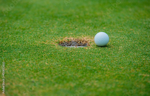 A white golf ball is placed in the mouth of the hole on the green grass