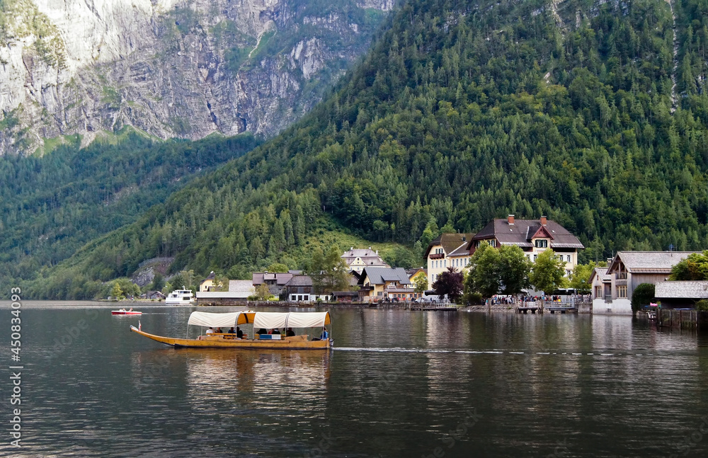Boat sailing in the lake of Hallstatt, with the Alpine mountains behind it.