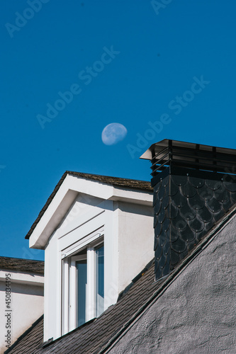 Window and black slate roofs with the moon and the blue sky on the background