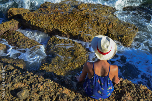 Beautiful young woman in a dress sitting by the sea in Spain.