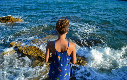Beautiful young woman in a dress sitting by the sea in Spain.