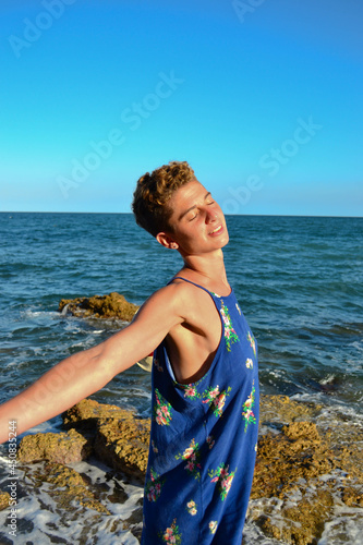 Beautiful young woman in a dress sitting by the sea in Spain.