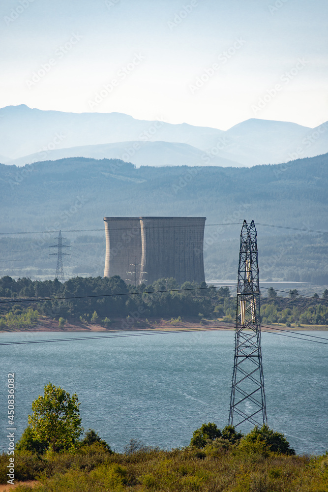 Fototapeta premium Two refrigeration towers from a power station next to a lake with some mountains on the background