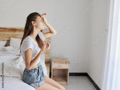 woman with medical mask on her face sitting on bed indoors isolation quarantine coronavirus vacation