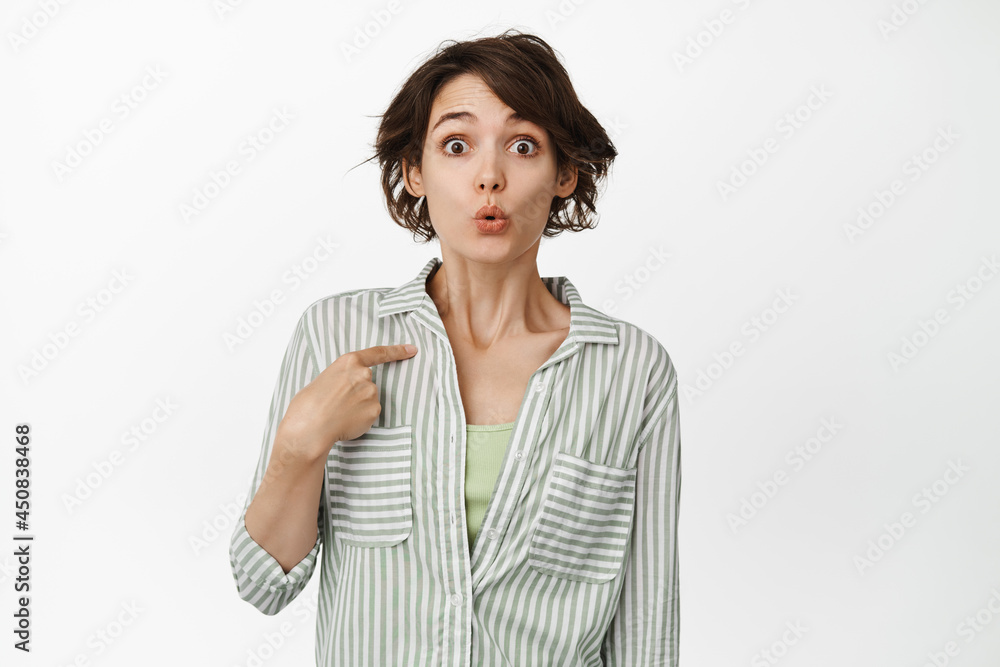 Surprised and intrigued young woman look amazed, pointing finger at herself, being chosen, picked for job, receive something interesting, standing against white background Surprised and intrigued young woman look amazed, pointing finger at herself, being chosen, picked for job, receive something interesting, standing against white background