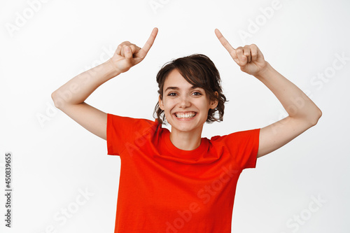 Portrait of happy smiling woman pointing fingers up, showing advertisement, give info, recommending website, white background