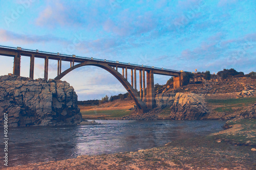 Very big and high stone bridge over a small river with a sunset sky photo