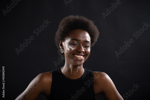 Beautiful young ethnic african american black woman applying moisturizer white cream on her face with emotion