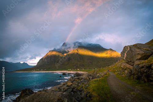 Scenic view on beach, rainbow and mountains against the sunset sky on the walking train to Unstad village, Lofoten, Norway