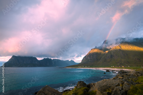 Scenic view on beach, rainbow and mountains against the sunset sky on the walking train to Unstad village, Lofoten, Norway © khomaviet