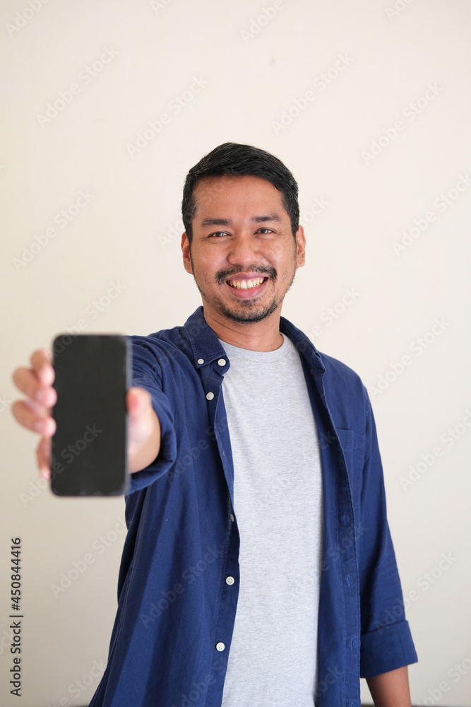 Adult Asian man smiling happy while showing blank mobile phone screen Adult Asian man smiling happy while showing blank mobile phone screen