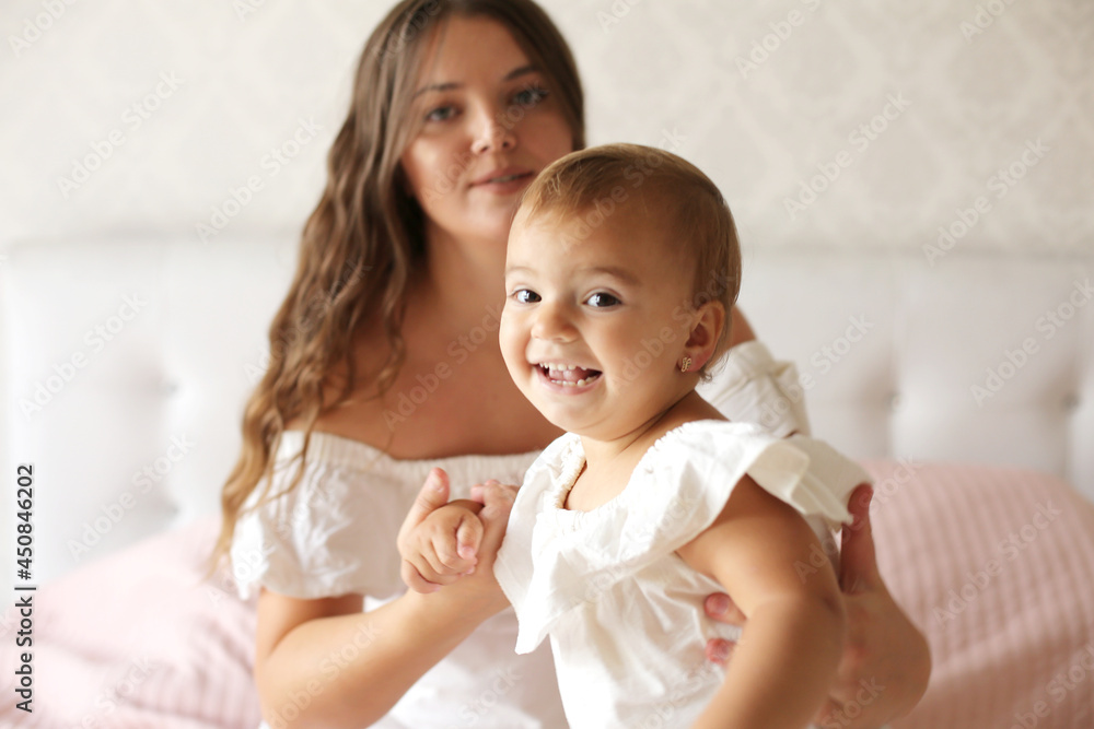 a young beautiful girl with dark long hair in a white dress hugs a small beautiful daughter on a pastel with a pink blanket a young beautiful girl with dark long hair in a white dress hugs a small beautiful daughter on a pastel with a pink blanket