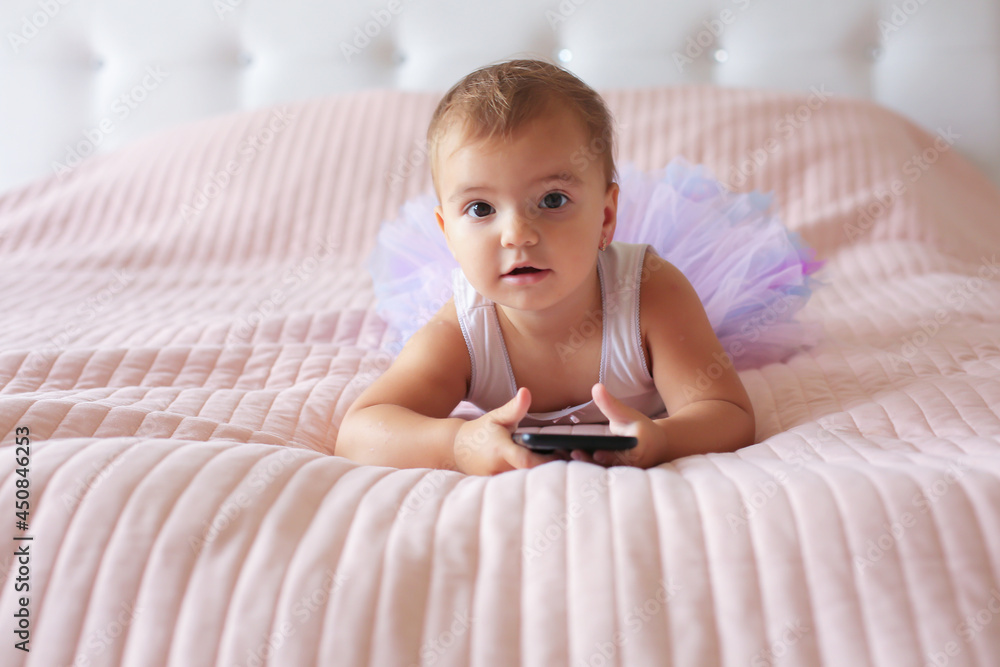 a little happy beautiful girl is lying on a pink blanket in a skirt and holding a phone in her hands a little happy beautiful girl is lying on a pink blanket in a skirt and holding a phone in her hands