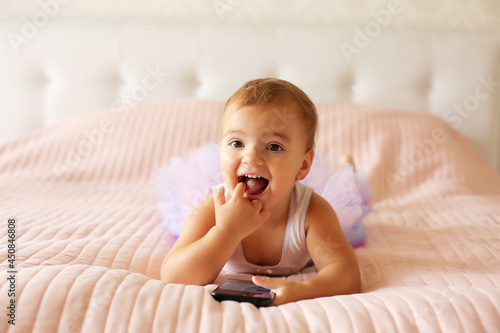 a little happy beautiful girl is lying on a pink blanket in a skirt and holding a phone in her hands