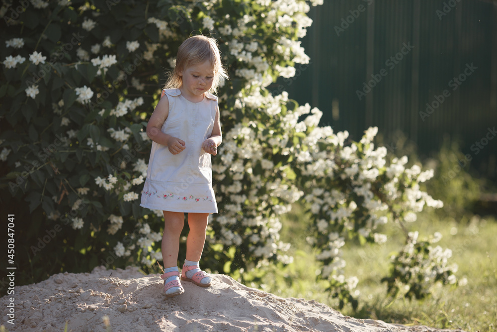 a little girl is standing on the sand, holding sand in her hands and examining it a little girl is standing on the sand, holding sand in her hands and examining it