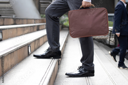 Business and grow up concept. Business man holding briefcase and walking up stairs going to work at morning in the city.