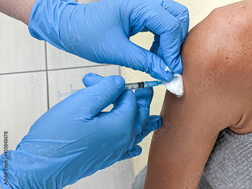 Close up of adult woman getting covid vaccine in clinic or hospital, with nurse injecting vaccine into shoulder