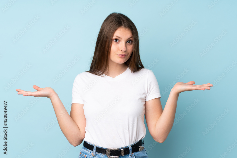 Teenager caucasian girl isolated on blue background making doubts gesture Teenager caucasian girl isolated on blue background making doubts gesture