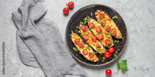 Baked eggplants with cherry tomato and cheese on a gray concrete background. Top view, flat lay, copy space. Wide composition