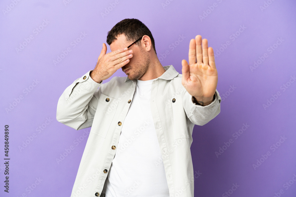 Brazilian man over isolated purple background making stop gesture and covering face Brazilian man over isolated purple background making stop gesture and covering face