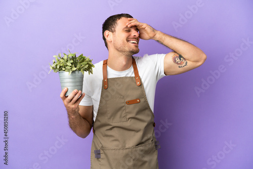 Brazilian Gardener man holding a plant over isolated purple background smiling a lot