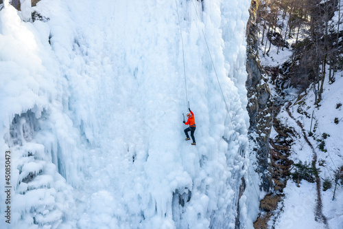 Aerial shot of a a Caucasian ice climber facing the slope, swinging ice axes and stepping up by kicking his toes in to plant the crampons