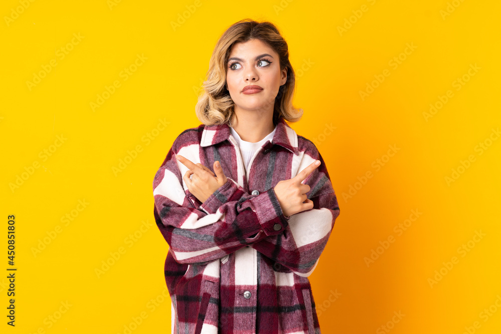 Young Russian woman isolated on yellow background pointing to the laterals having doubts Young Russian woman isolated on yellow background pointing to the laterals having doubts