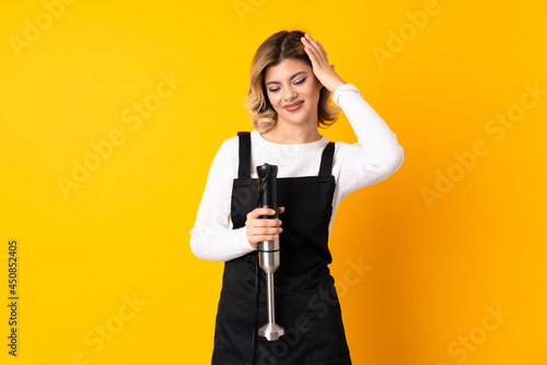 Girl using hand blender isolated on yellow background laughing