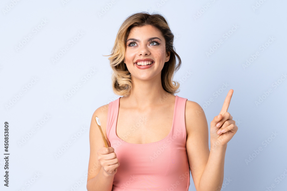 Teenager girl brushing her teeth isolated on blue background intending to realizes the solution while lifting a finger up Teenager girl brushing her teeth isolated on blue background intending to realizes the solution while lifting a finger up