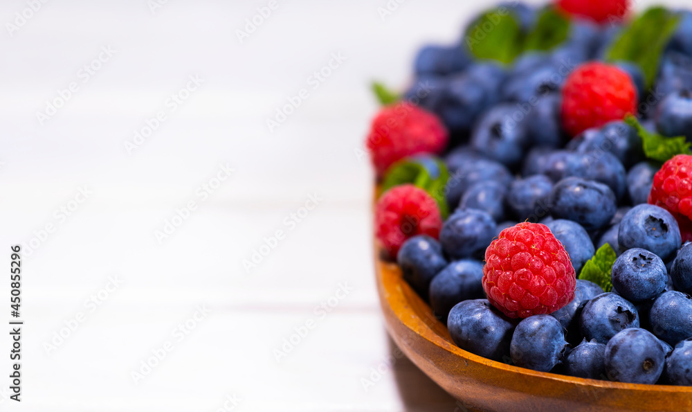 Blueberry and Raspberry With a Green Mint leaf in a Wooden Bowl on a white top view, Summer Freshly Berry, Copyspace Blueberry and Raspberry With a Green Mint leaf in a Wooden Bowl on a white top view, Summer Freshly Berry, Copyspace