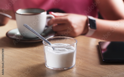 Woman holding a cup of coffee with milk and next to the sweetener