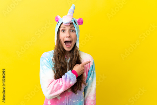 Girl with unicorn pajamas over isolated background surprised and pointing side