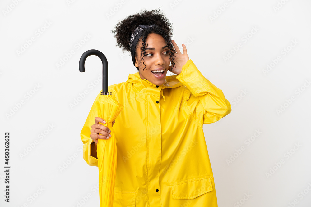 Young woman with rainproof coat and umbrella isolated on white background listening to something by putting hand on the ear Young woman with rainproof coat and umbrella isolated on white background listening to something by putting hand on the ear
