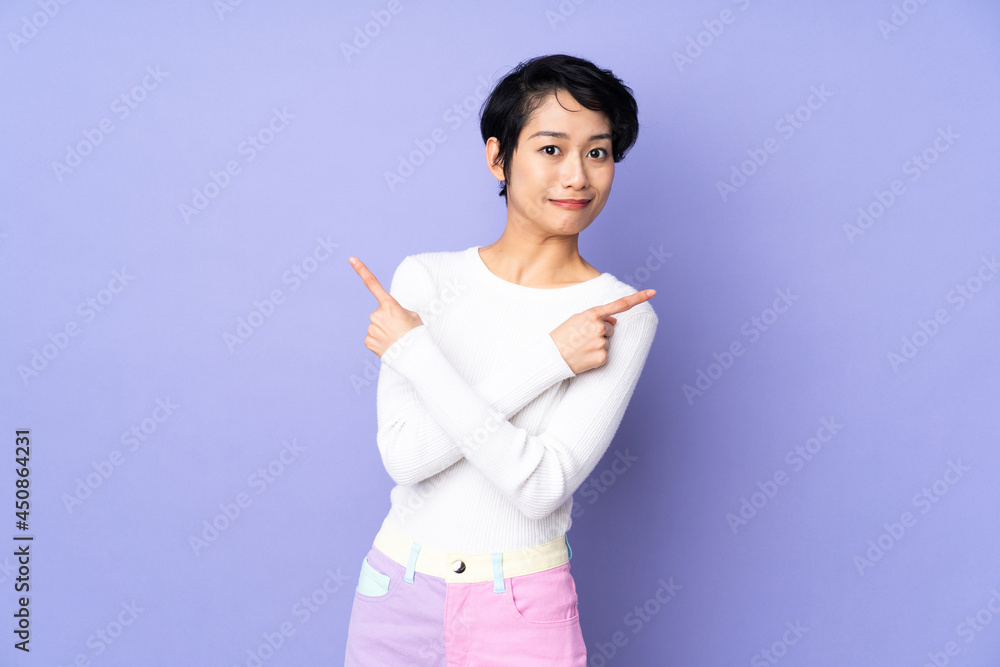 Young Vietnamese woman with short hair over isolated purple background pointing to the laterals having doubts Young Vietnamese woman with short hair over isolated purple background pointing to the laterals having doubts