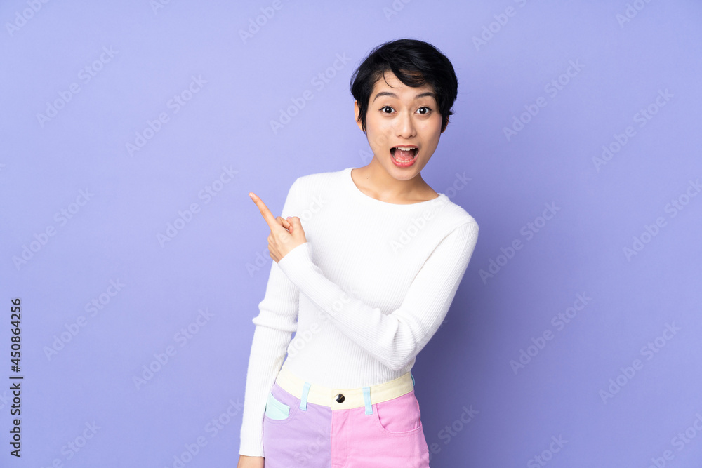 Young Vietnamese woman with short hair over isolated purple background surprised and pointing side Young Vietnamese woman with short hair over isolated purple background surprised and pointing side